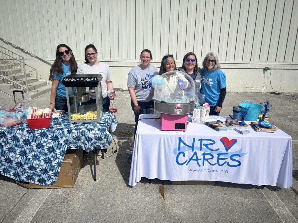 Group of women stand behind an NRV CARES table at an outdoor event, doling out popcorn and cotton candy to attendees