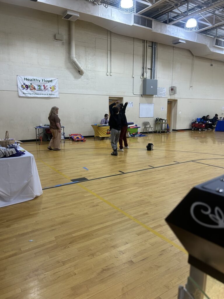 In a gymnasium, event attendees dance in the middle of the wooden floor