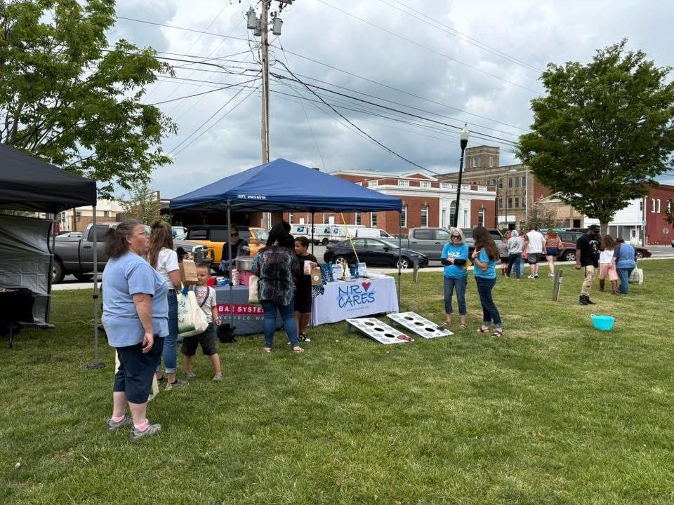 Event attendees gather on the grass outside an NRV Cares tent to play cornhole 