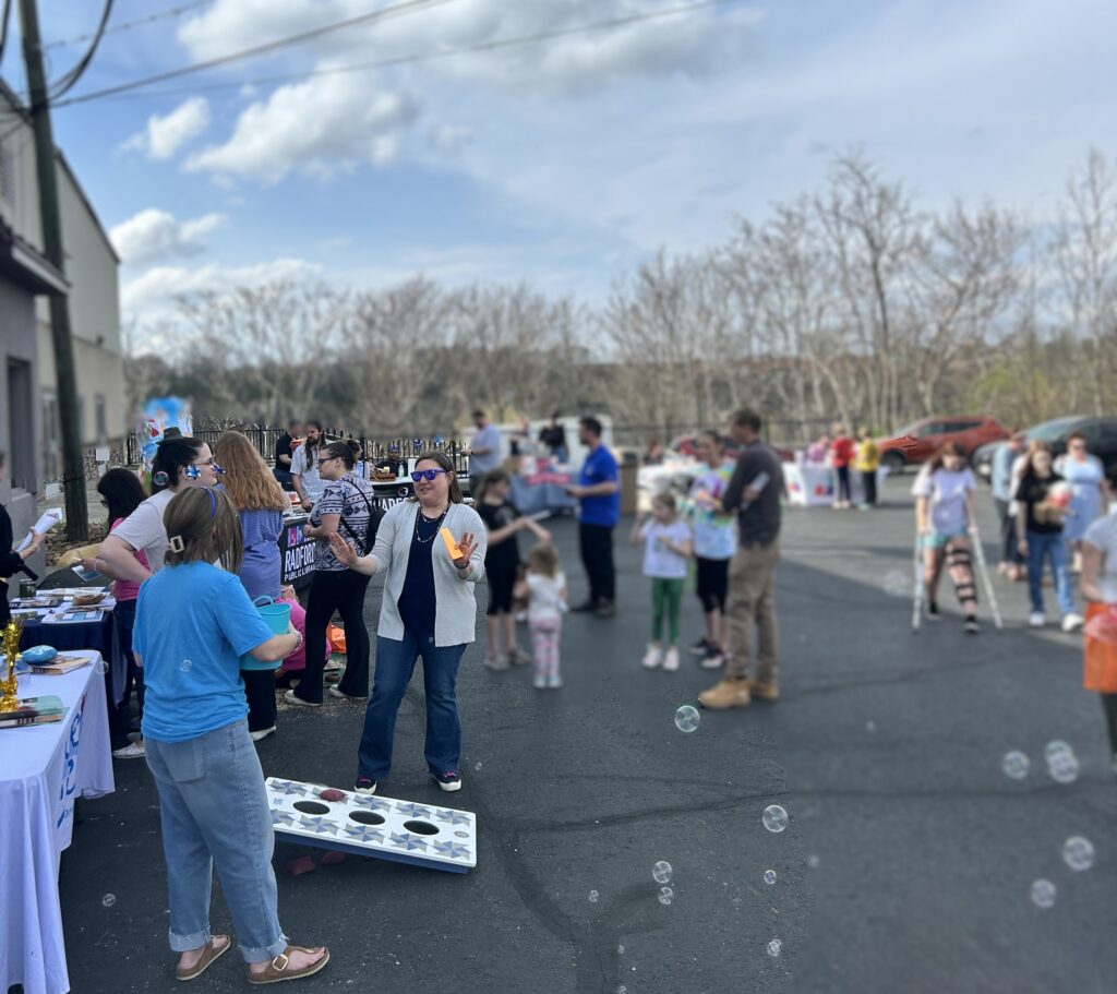 Event attendees blow bubbles and stand near cornhole boards in a parking lot 